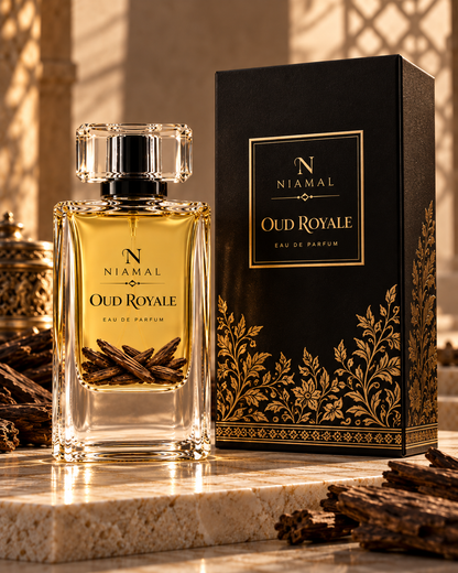 A clear glass perfume bottle filled with amber-gold liquid stands beside a tall black box with gold ornamental detailing. The labels read Niamal and Oud Royale Eau de Parfum.